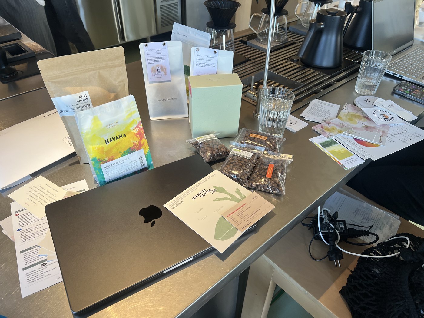 A laptop, bags of coffee beans, and brewing equipment on a coffee shop counter